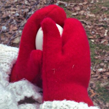 pair of little hands wearing red wool mittens holding an egg