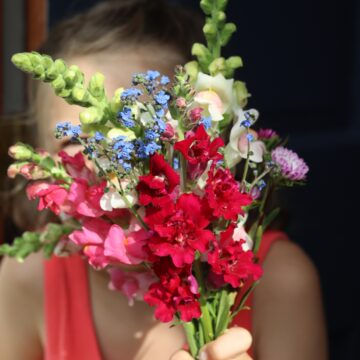 little girl holding big bouquet of flowers in front of her face