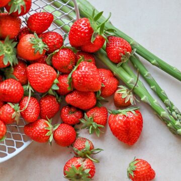 strawberries and asparagus spilling from a white basket onto a table