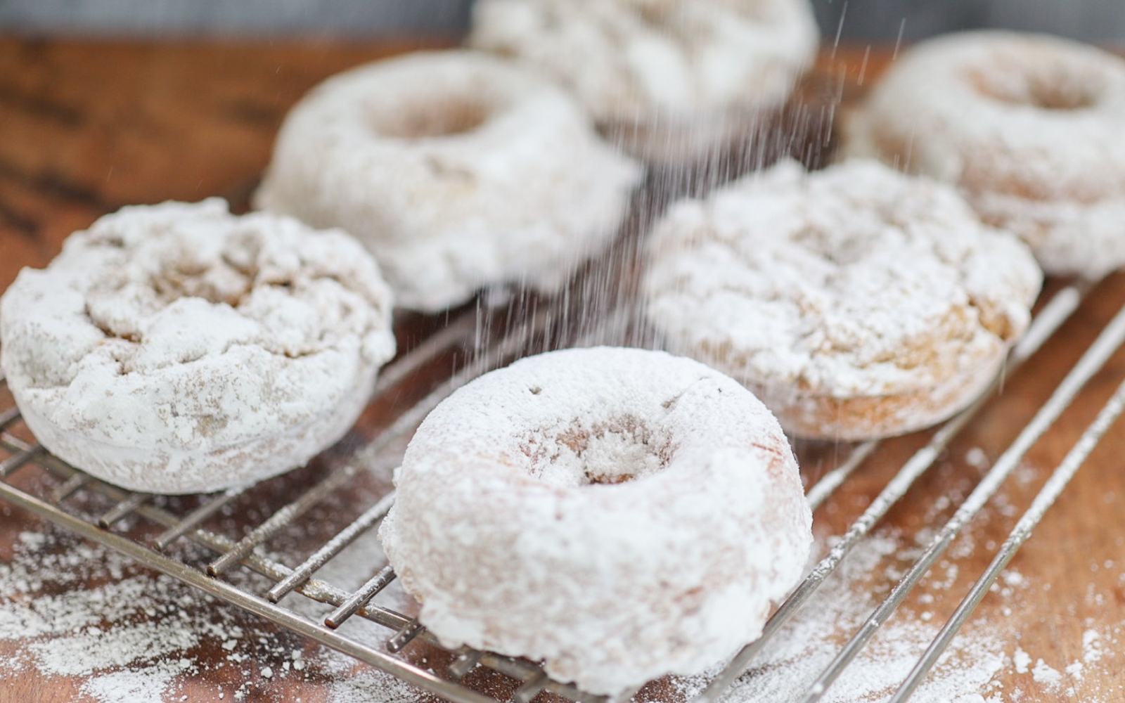 donuts on a cooling rack being sprinkled with powdered sugar