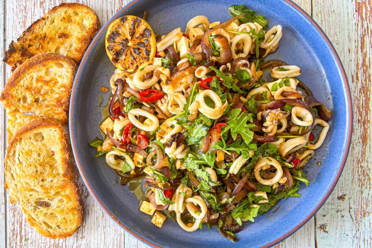 sautéed calamari salad in a blue bowl with grilled bread