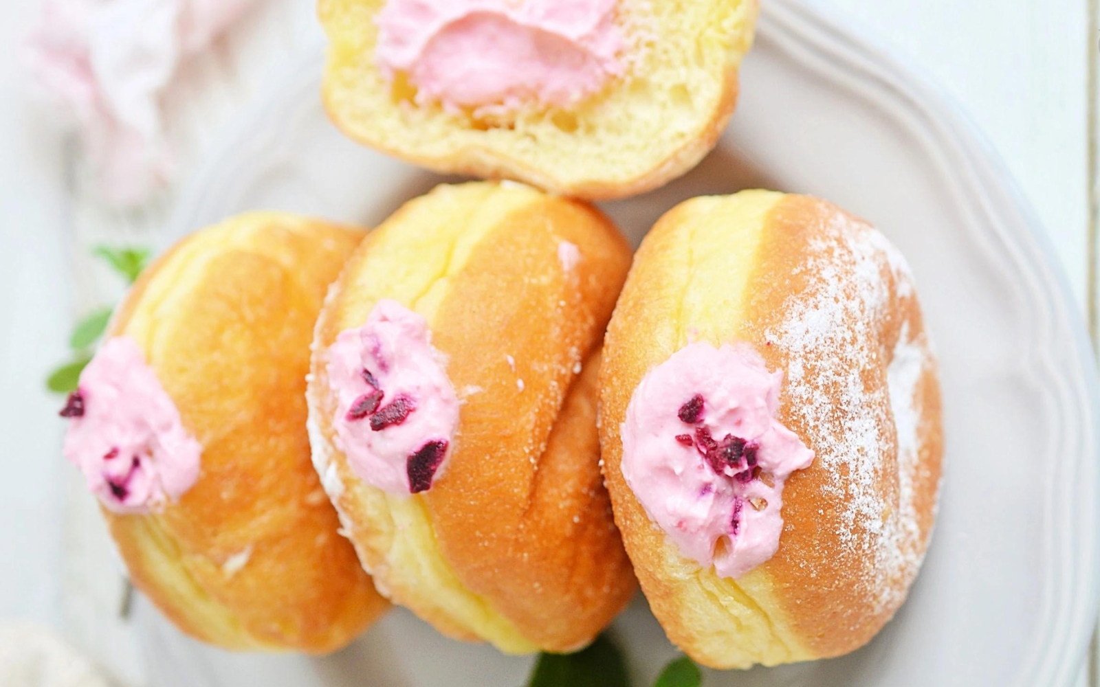a plate of brioche donuts with pink raspberry cheesecake filling