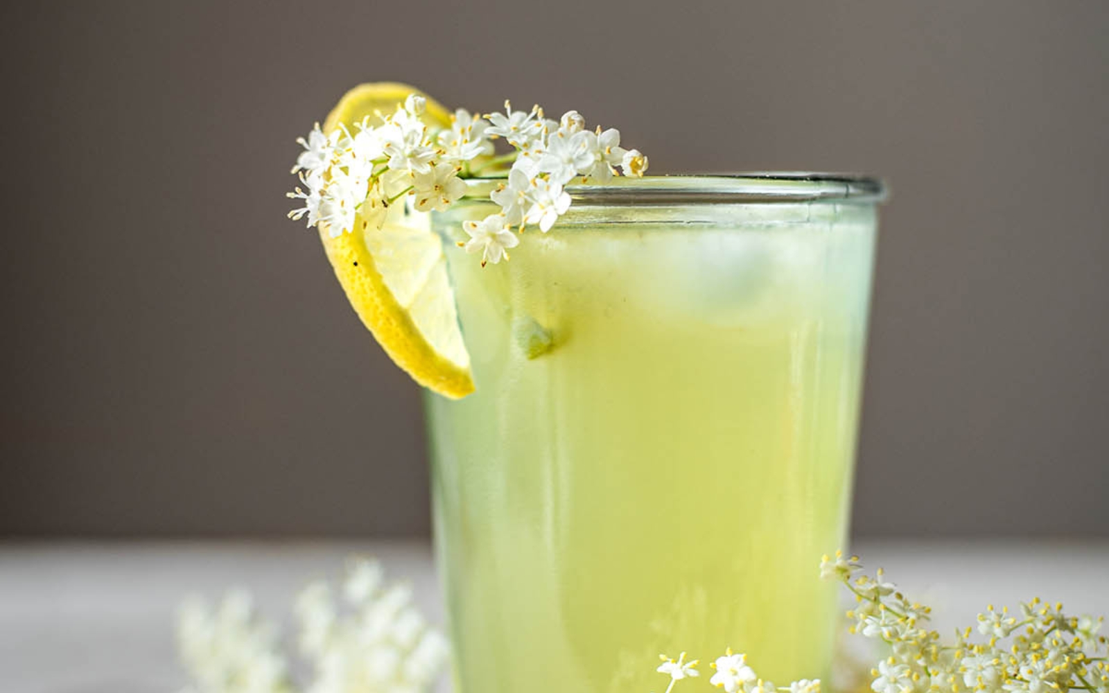glass of elderflower lemonade with lemon slice and elderflower blossoms