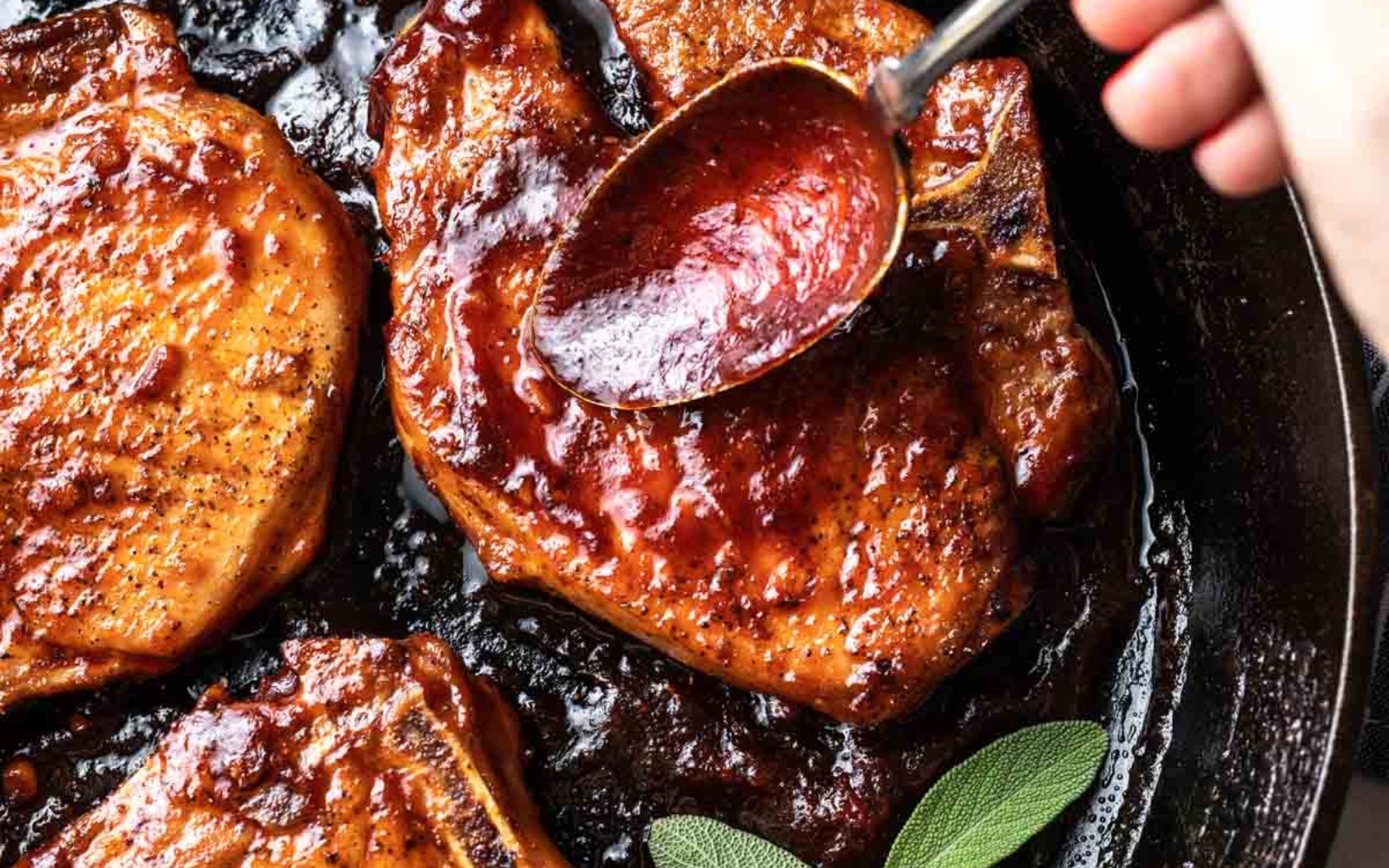 pork chops in a cast iron pan being slathered with harissa maple sauce