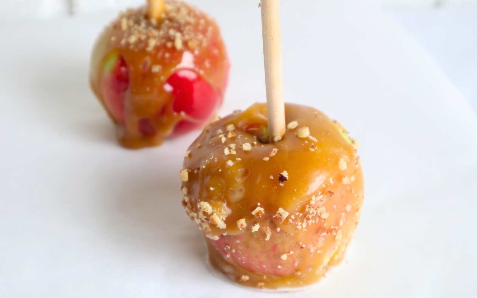 two caramel apples with ground nuts on them