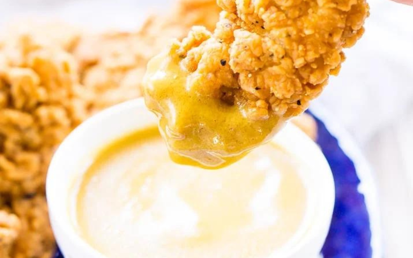 crispy chicken being dipped into maple mustard sauce