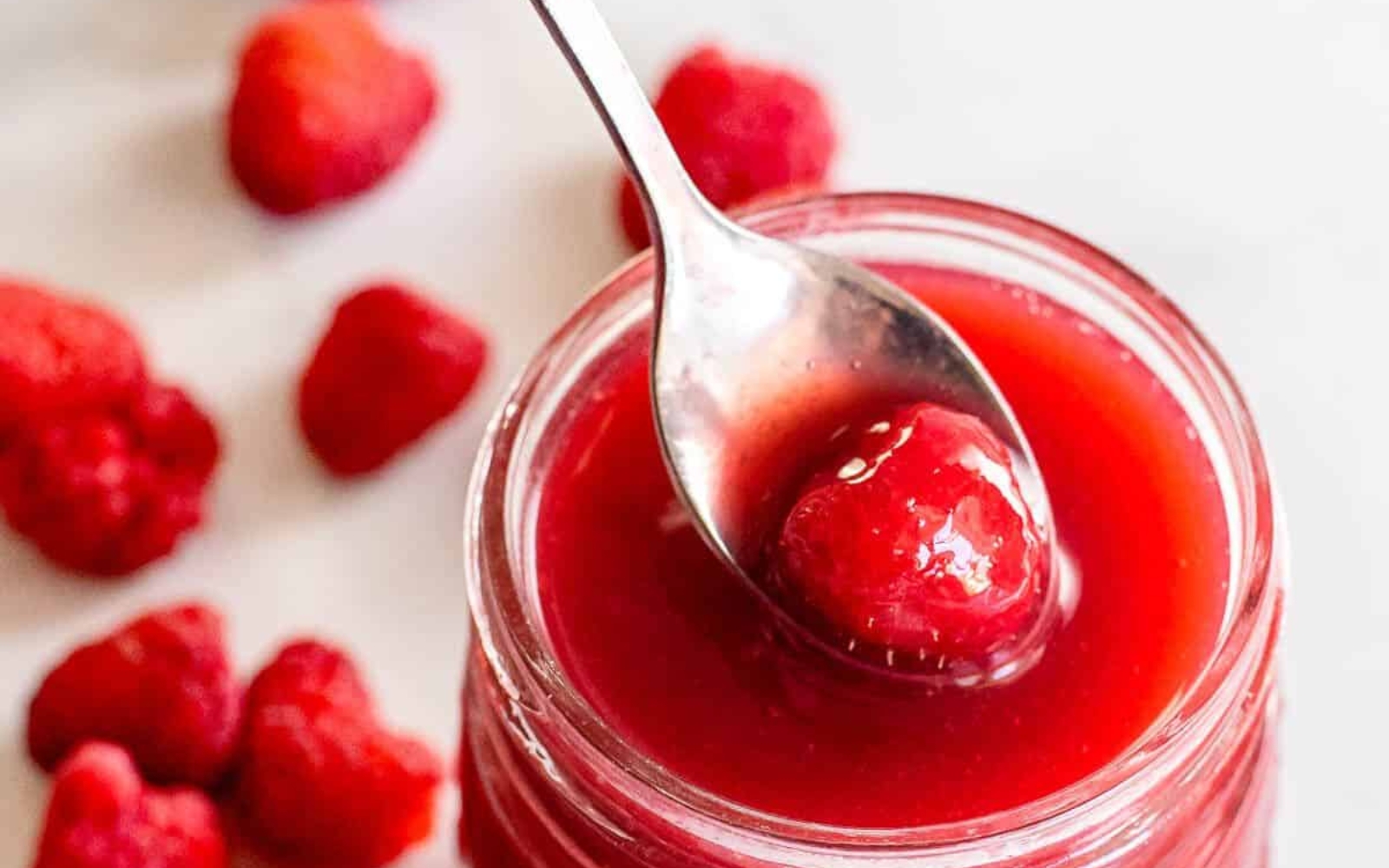 a jar of raspberry sauce with spoon