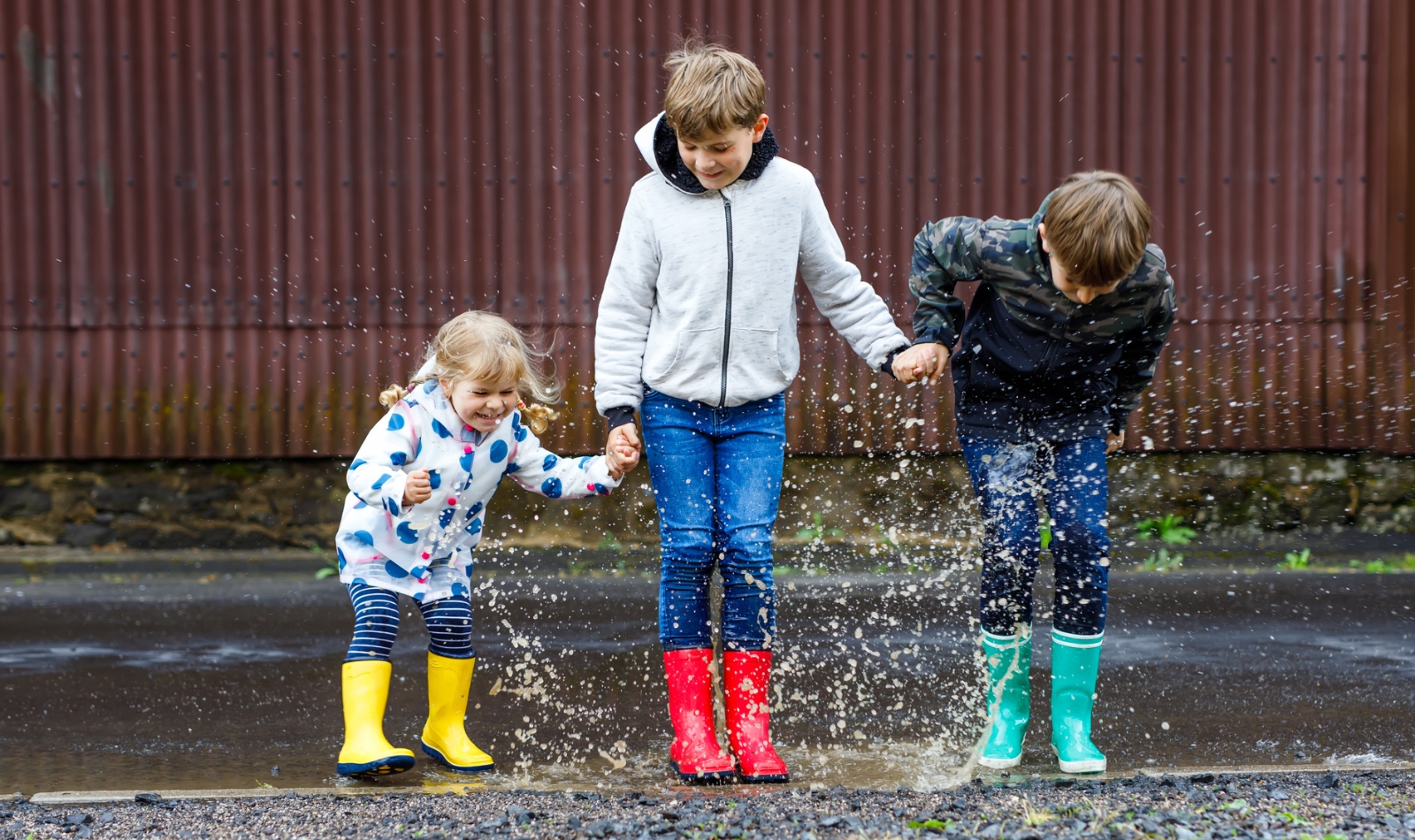 three kids with rain boots jumping in a puddle