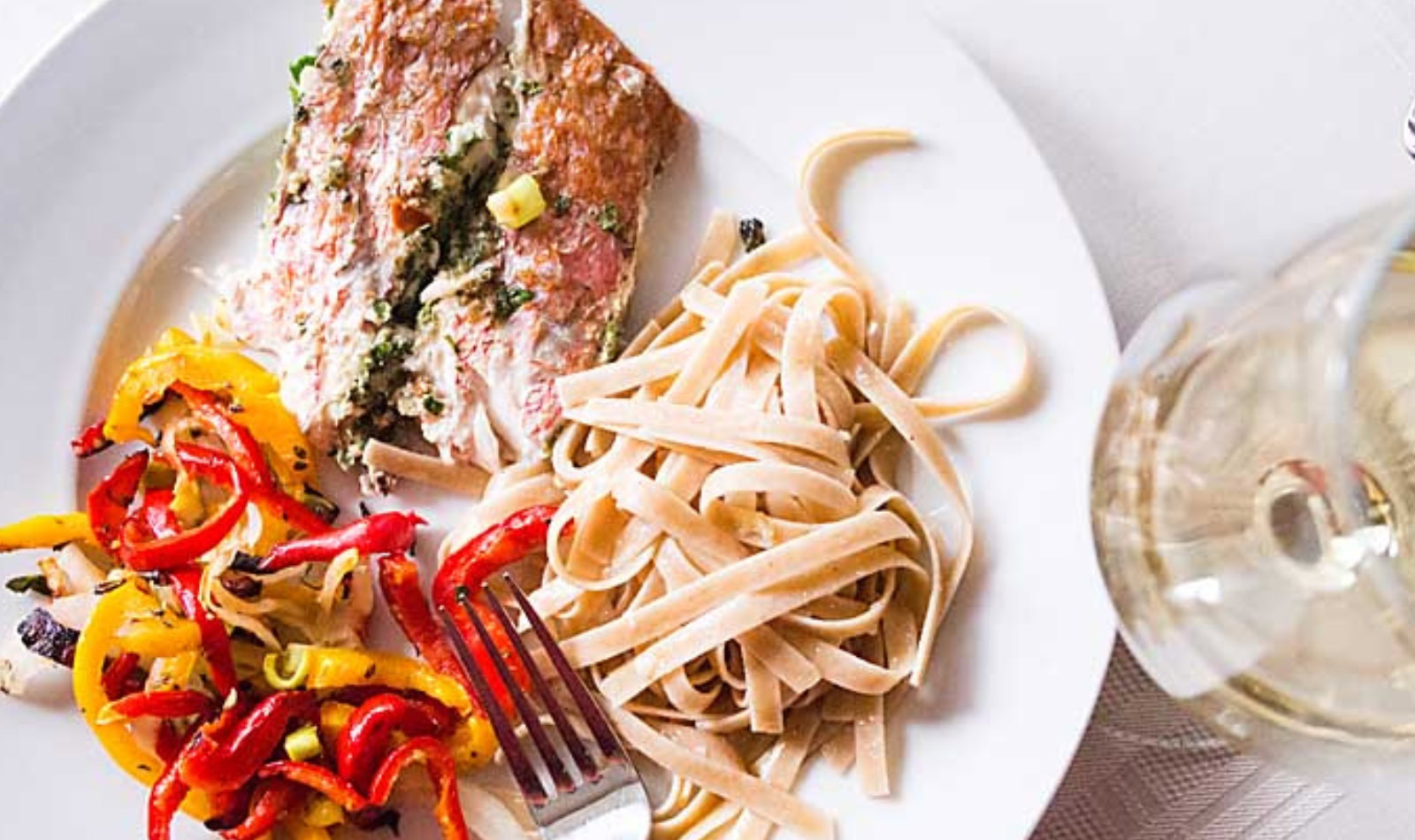 grilled red snapper on a plate with grilled peppers and fettuccini