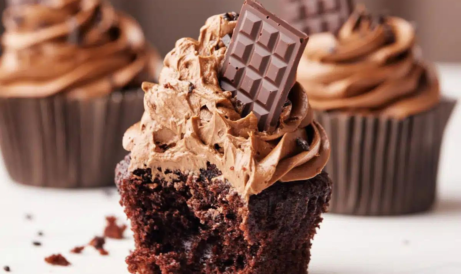 image of Chocolate Cupcakes with Silky Chocolate Buttercream frosting and a slice of chocolate bar on top.