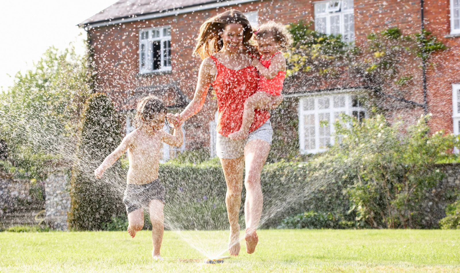 mom and kids running through a sprinkler