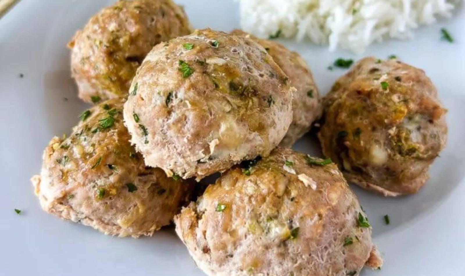 turkey-zucchini-meatballs on a white plate with white rice and some sprinkled green herbs