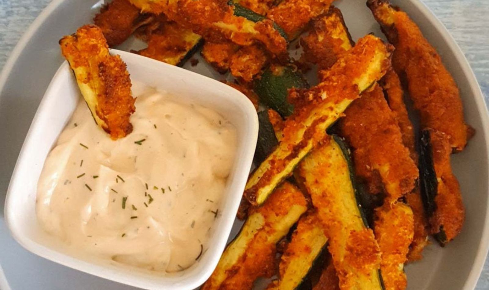 Image of crispy air fryer zucchini fries with a white bowl of creamy white dip on a white plate.